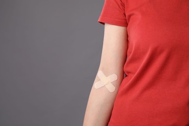 Photo of Blood donation. Woman with sticking plaster on her arm against grey background, closeup. Space for text