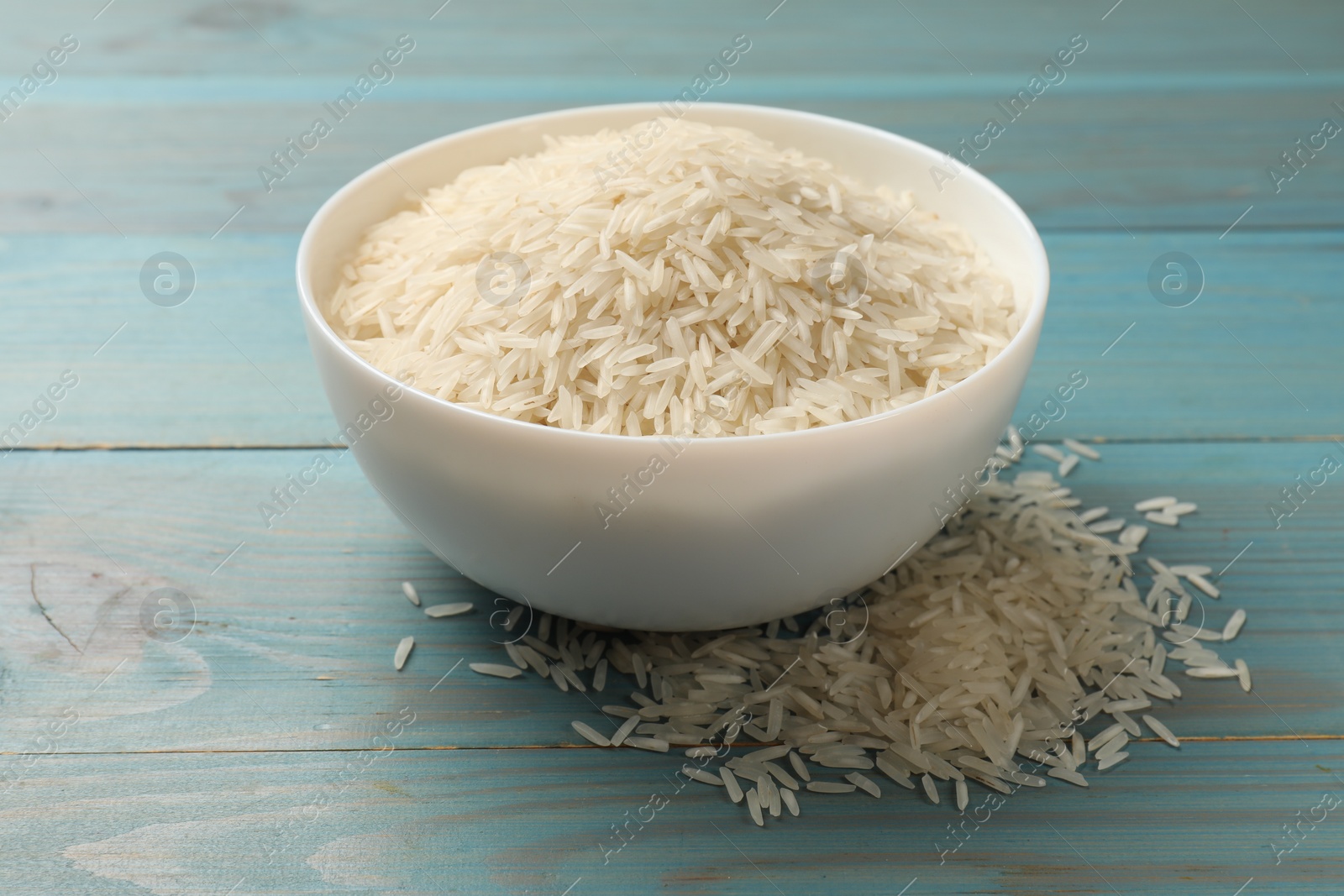 Photo of Raw basmati rice in bowl on light blue wooden table