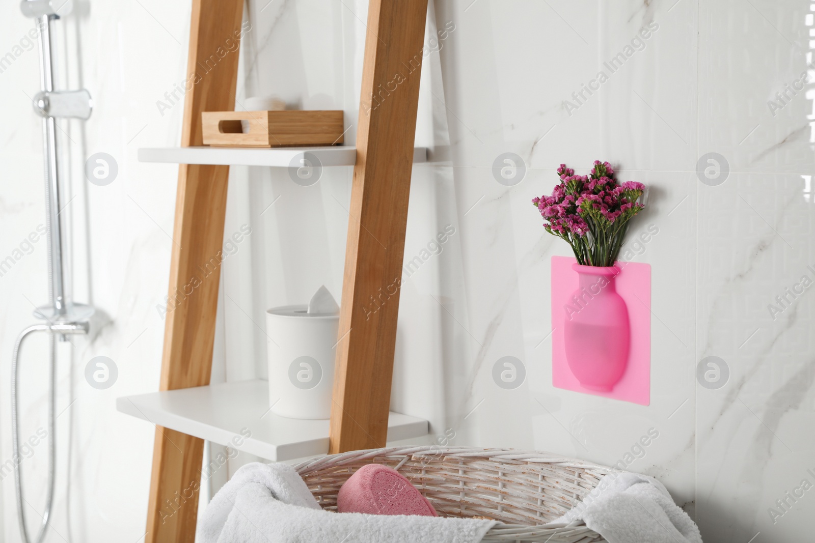 Photo of Silicone vase with flowers on white marble wall in stylish bathroom