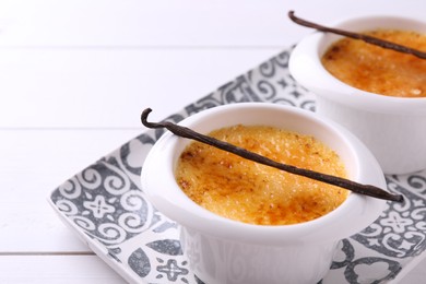 Photo of Delicious creme brulee in bowls and vanilla pods on white wooden table, closeup