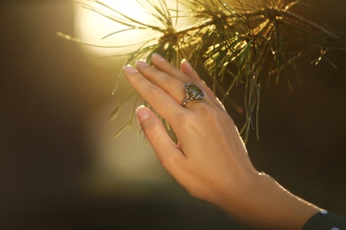 Young woman wearing beautiful silver ring with prehnite gemstone near pine, closeup