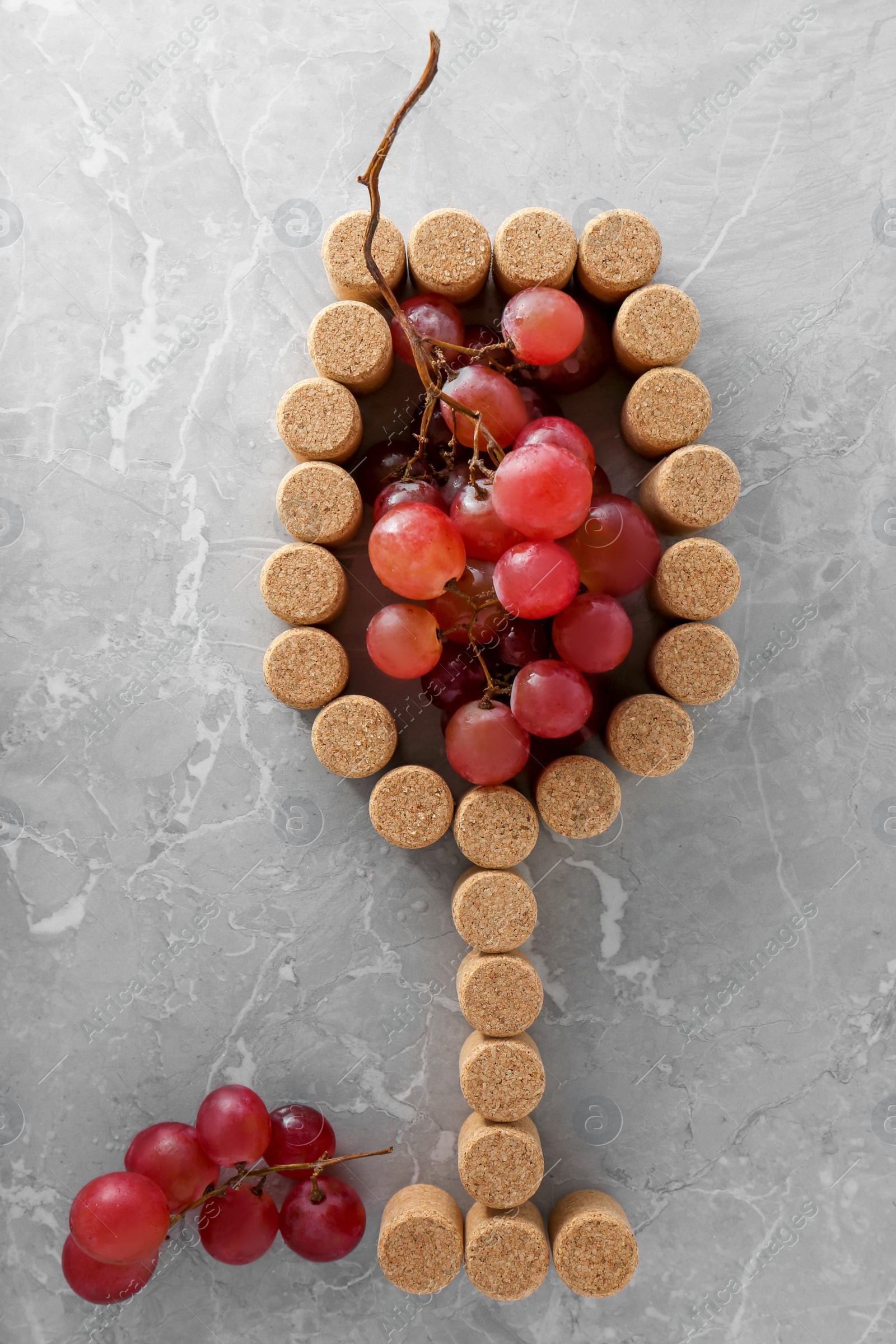 Photo of Glass of wine made with bottle corks and grapes on grey table, flat lay