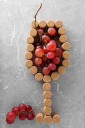 Glass of wine made with bottle corks and grapes on grey table, flat lay