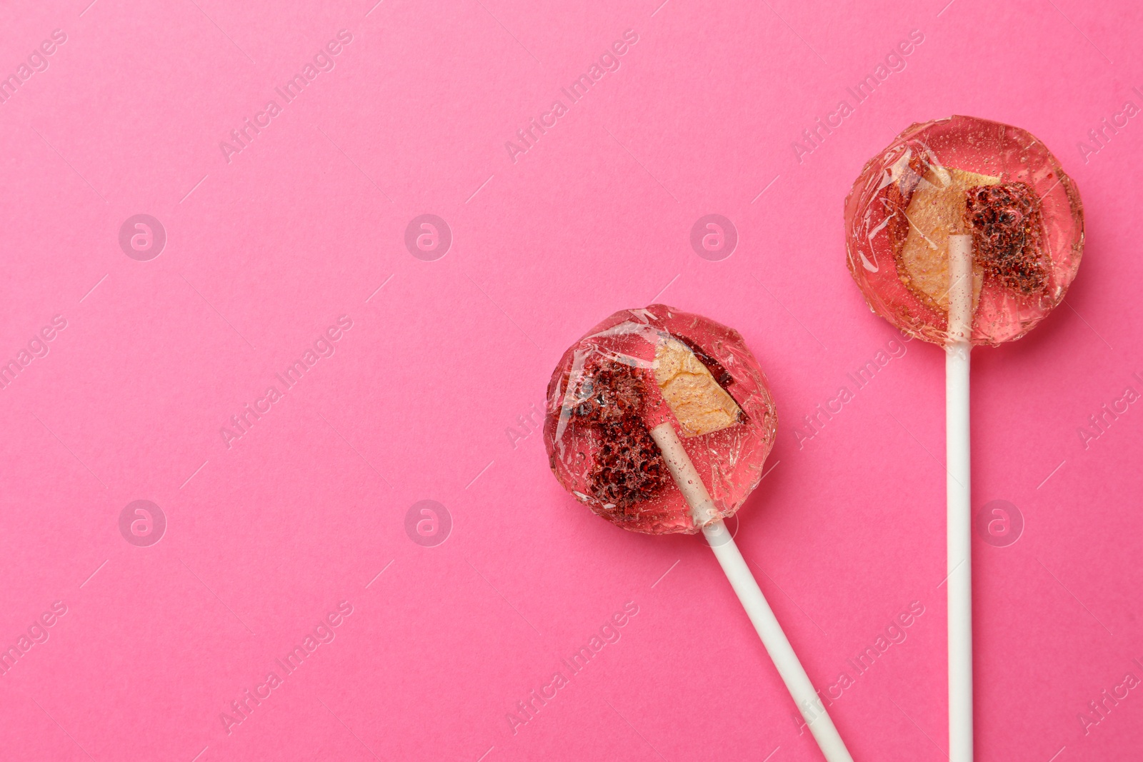 Photo of Sweet colorful lollipops with berries on pink background, flat lay. Space for text