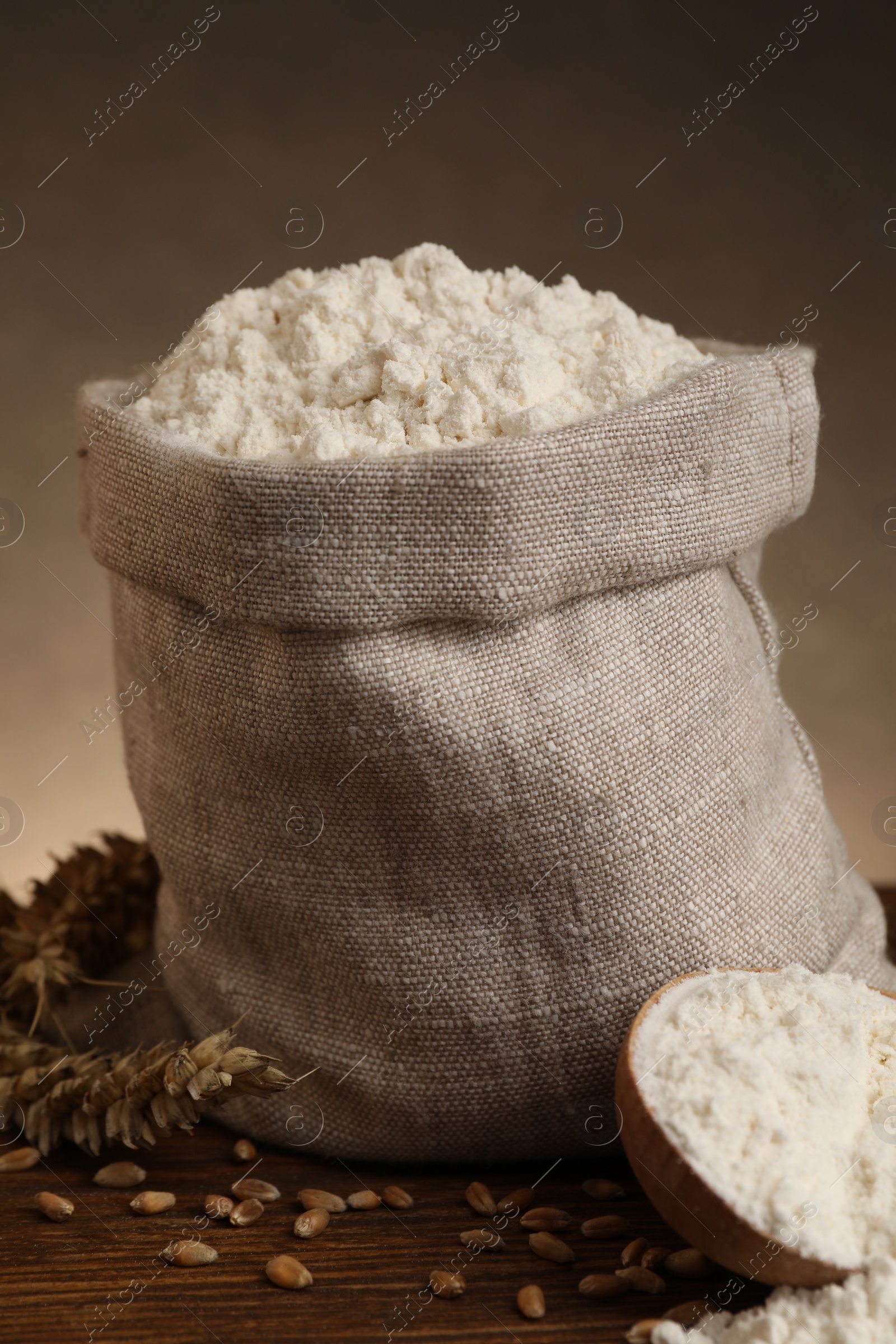 Photo of Wheat flour, grains and spikes on wooden table, closeup