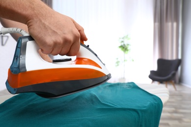 Photo of Man ironing clothes on board at home, closeup