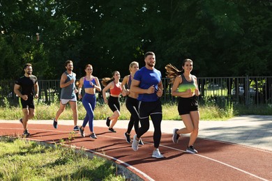 Group of people running at stadium on sunny day