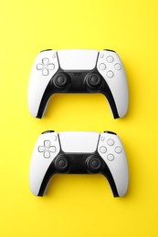 Photo of Wireless game controllers on yellow background, flat lay