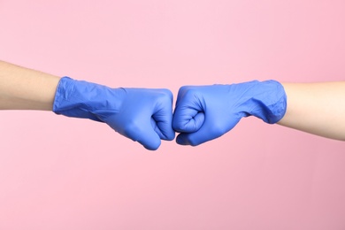 Photo of People in medical gloves doing fist bump on pink background, closeup of hands