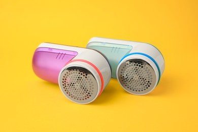 Modern fabric shavers in different colors on yellow background, closeup
