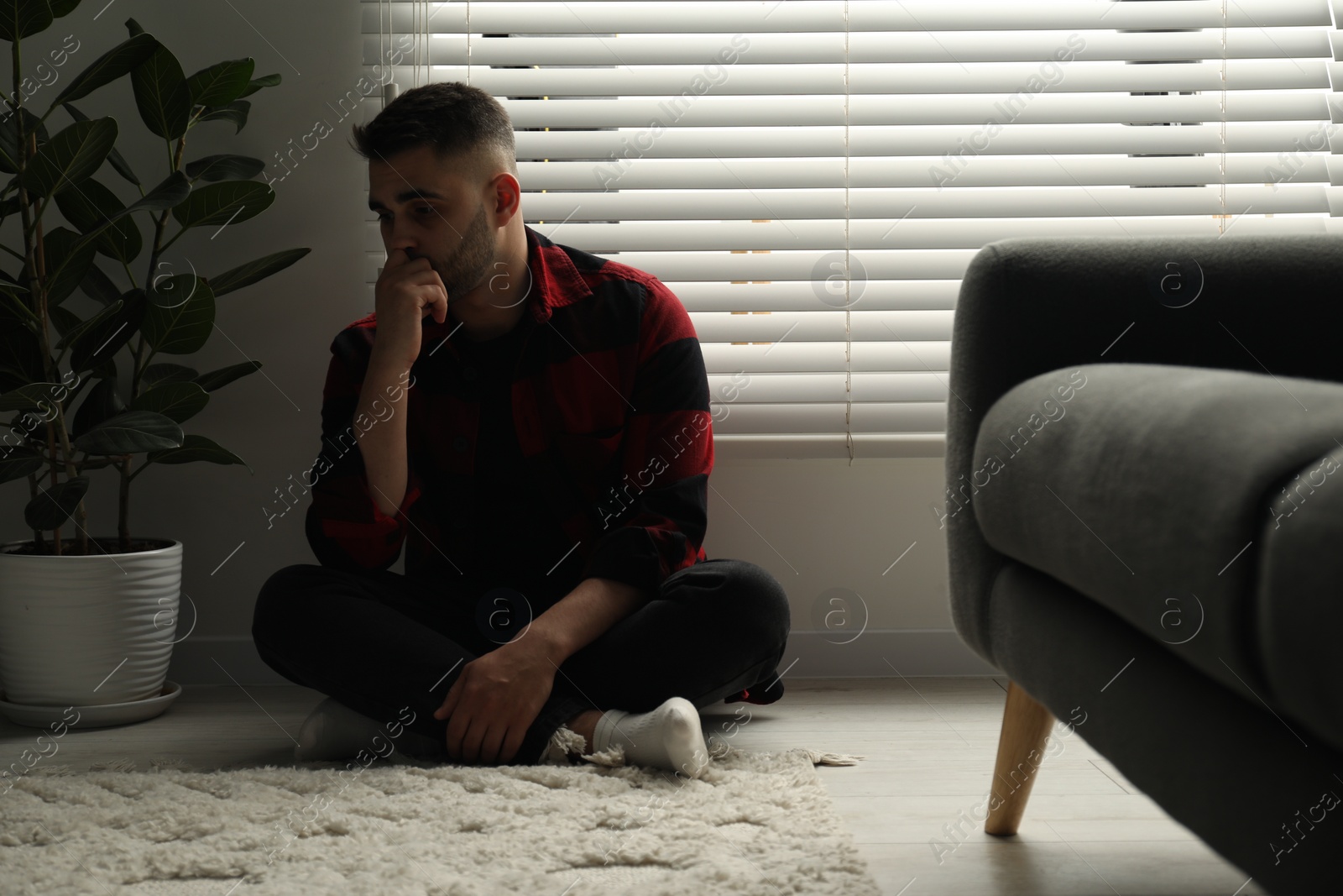 Photo of Sad man sitting near closed blinds indoors