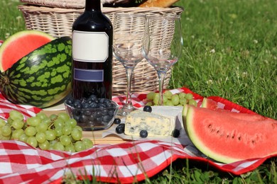 Picnic blanket with delicious food and wine outdoors on sunny day, closeup