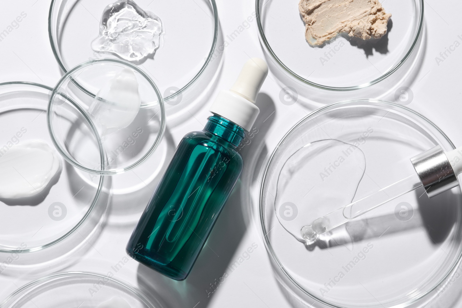 Photo of Bottle of cosmetic serum and petri dishes with samples on white background, flat lay