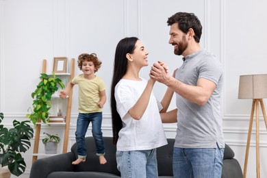 Photo of Happy family having fun in living room. Couple dancing while their son jumping on sofa