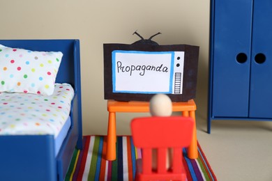 Propaganda concept. Wooden figure in front of paper TV in toy room