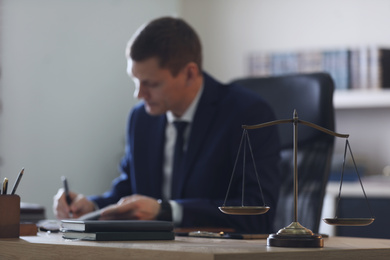 Photo of Male lawyer working at table in office, focus on scales of justice