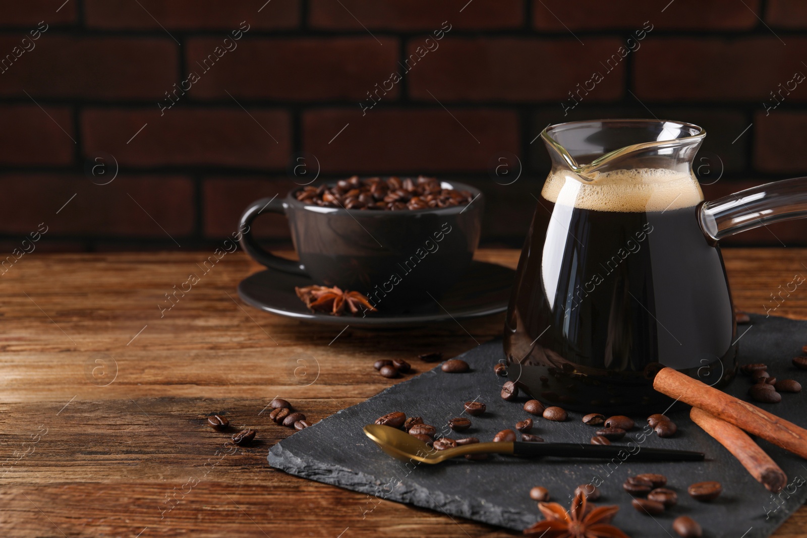 Photo of Turkish coffee in glass cezve, beans and spices on wooden table. Space for text