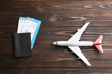 Toy airplane and passport with tickets on wooden background, flat lay