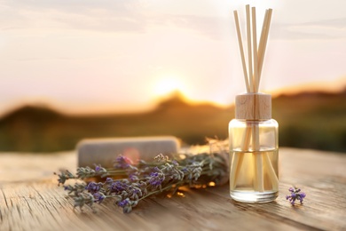Photo of Reed air freshener with oil and fresh lavender flowers on wooden table outdoors. Space for text