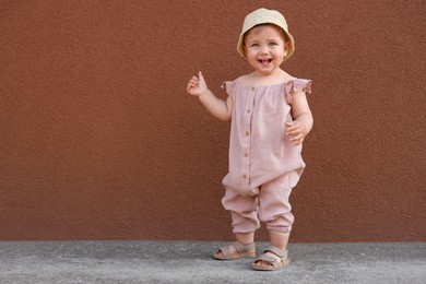 Photo of Cute little girl wearing stylish clothes near brown wall outdoors. Space for text