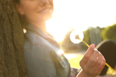 Young woman with dandelion in park on sunny day, closeup. Allergy free concept