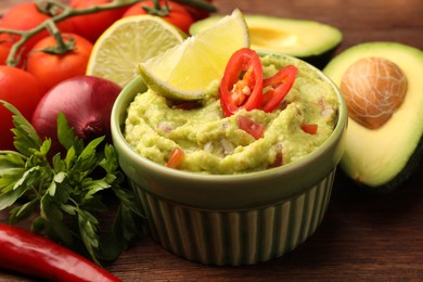 Photo of Bowl of delicious guacamole and ingredients on wooden table, closeup