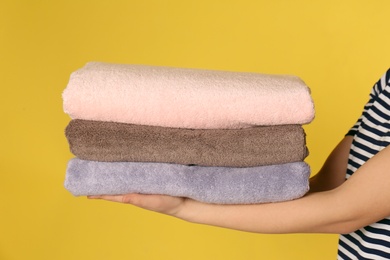 Photo of Young woman holding clean laundry on color background, closeup