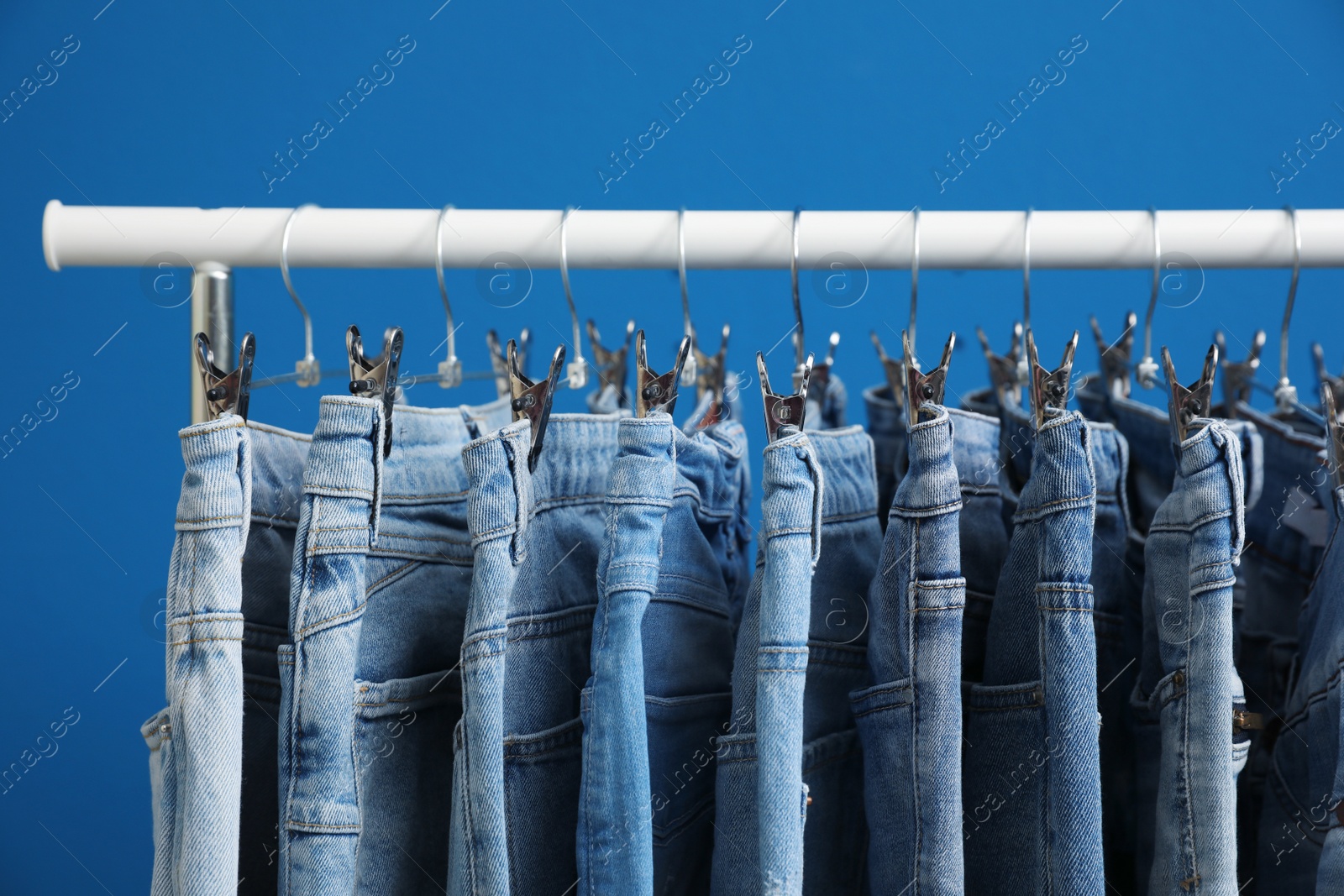 Photo of Rack with stylish jeans on blue background, closeup