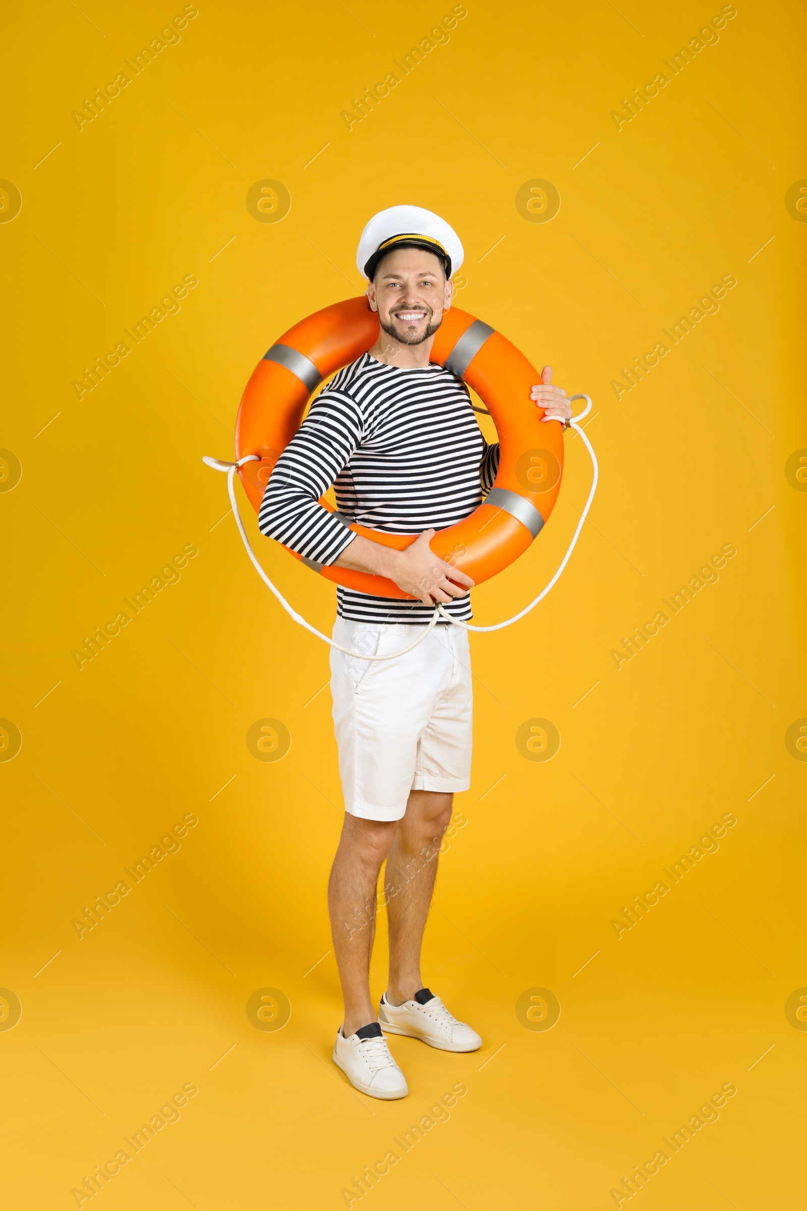 Photo of Happy sailor with orange ring buoy on yellow background