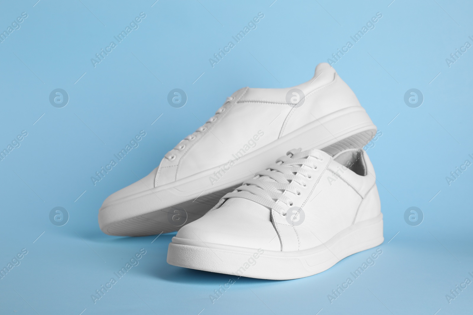 Photo of Pair of stylish white sneakers on light blue background