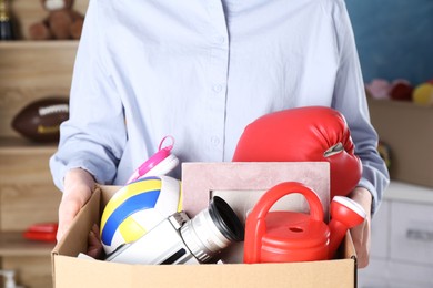 Woman holding box of unwanted stuff indoors, closeup