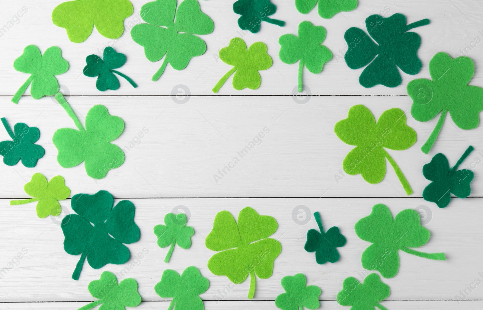 Photo of St. Patrick's day. Frame of green decorative clover leaves on white wooden table, flat lay. Space for text