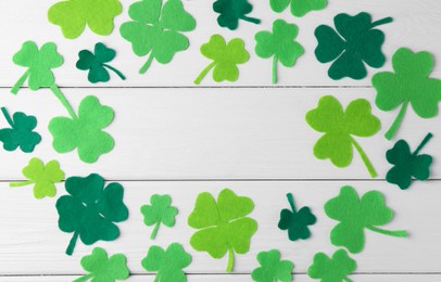 St. Patrick's day. Frame of green decorative clover leaves on white wooden table, flat lay. Space for text