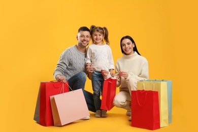 Photo of Happy family with paper bags on yellow background. Christmas shopping