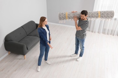Photo of Smiling couple holding rolled carpet in room