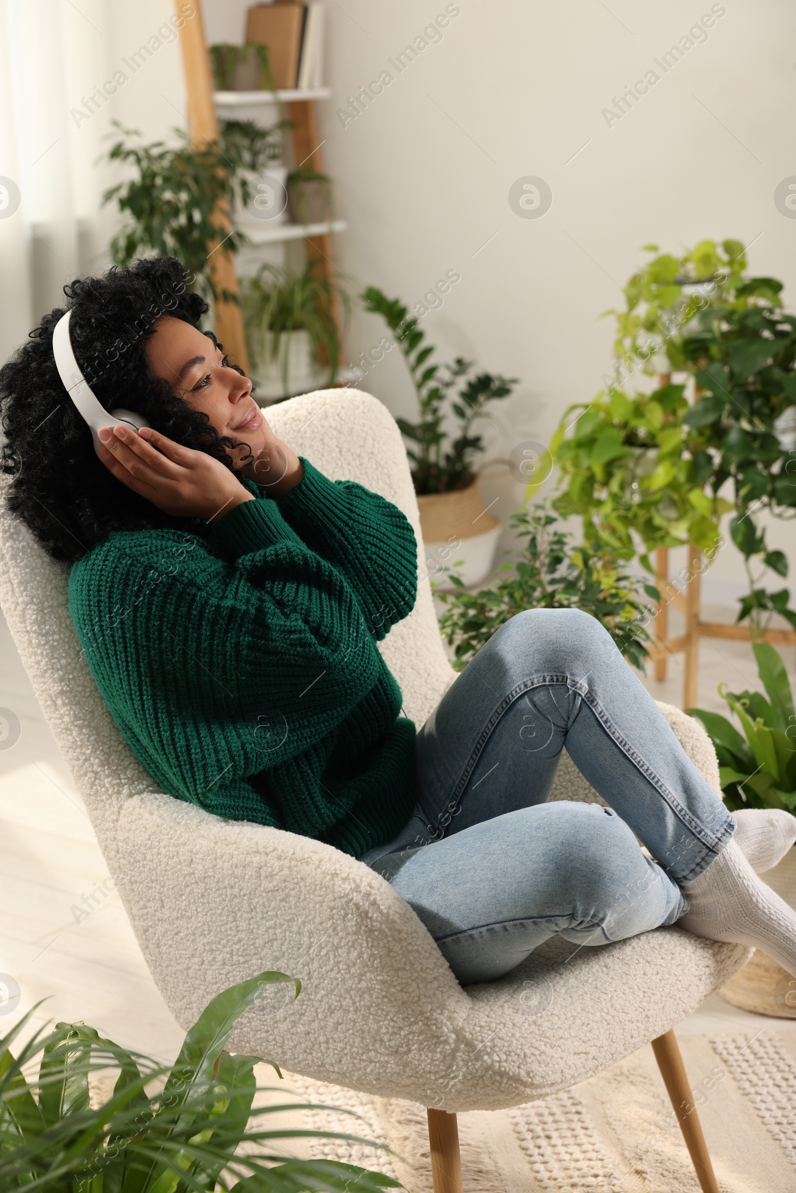 Photo of Relaxing atmosphere. Woman wearing headphones and listening music in room with beautiful houseplants
