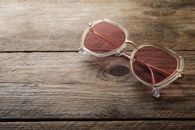 Photo of New stylish sunglasses on wooden table, space for text