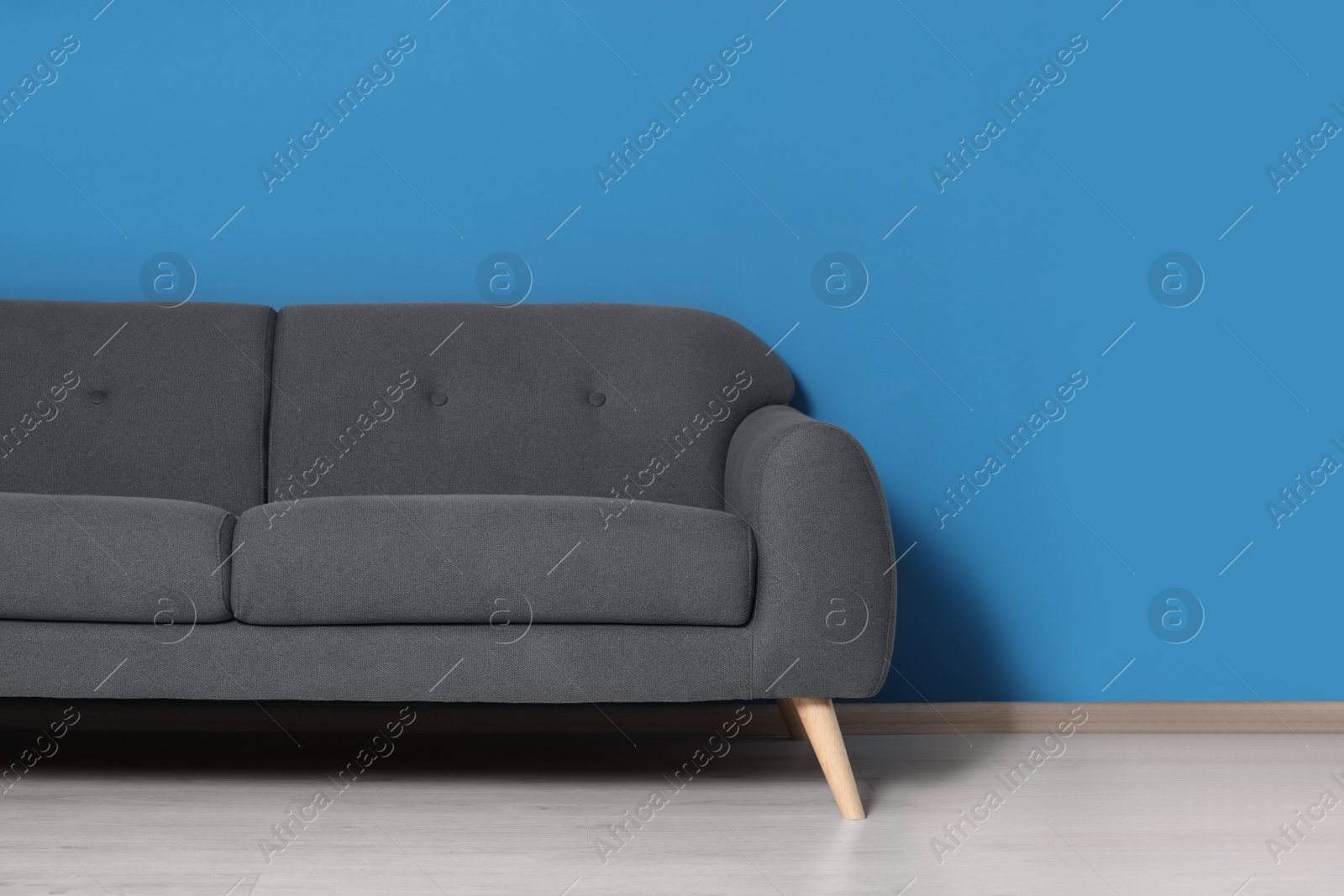 Photo of Stylish grey sofa near blue wall in room. Interior design