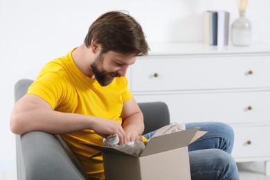 Photo of Happy man opening parcel at home. Internet shopping