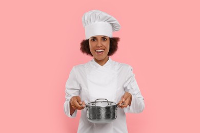 Photo of Happy female chef in uniform holding cooking pot on pink background