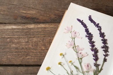 Photo of Open book with beautiful dried flowers on wooden table, top view. Space for text