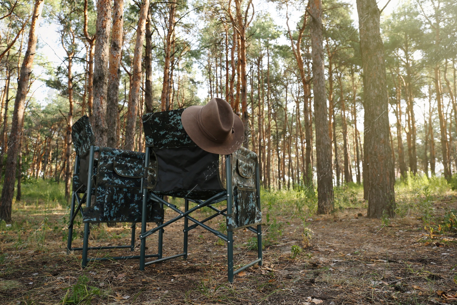 Photo of Camouflage chairs with hat in forest on sunny day