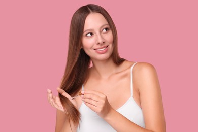Photo of Beautiful woman applying serum onto hair on pink background