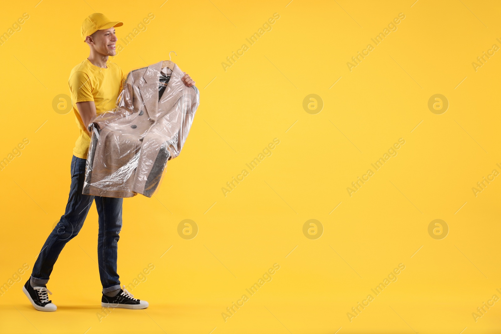 Photo of Dry-cleaning delivery. Happy courier holding coat in plastic bag on orange background, space for text