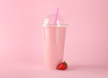 Photo of Plastic cup of tasty smoothie and fresh strawberry on pink background