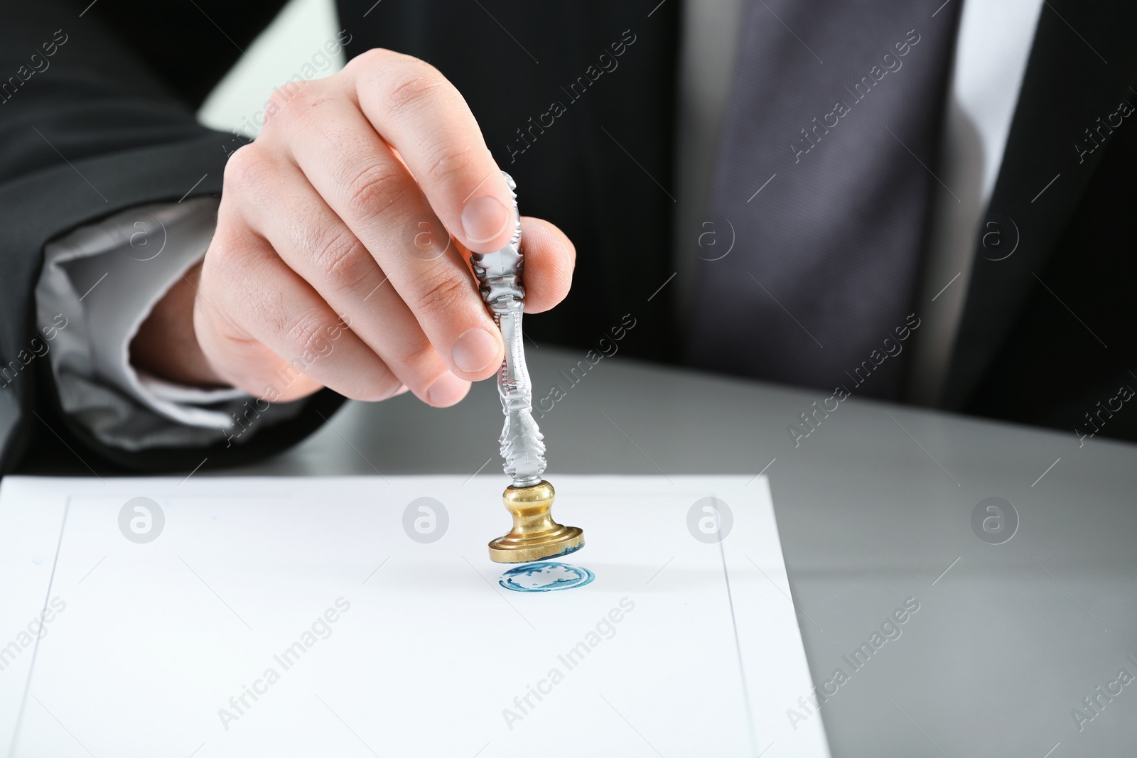 Photo of Male notary stamping document at table, closeup