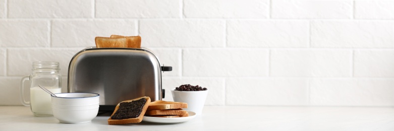 Photo of Modern toaster and delicious breakfast on table near brick wall, space for text. Banner design