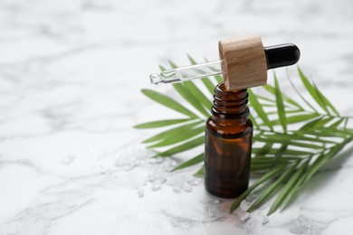 Photo of Bottle of essential oil and green twig on white marble table, closeup. Space for text
