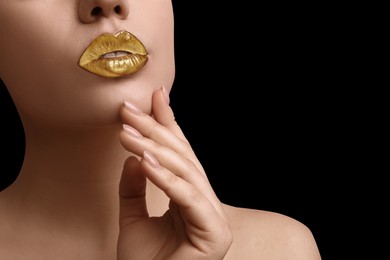 Image of Young woman with beautiful gold lips on black background, closeup. Space for text