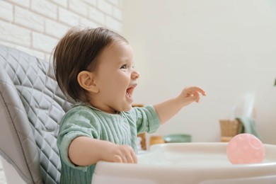 Cute little baby sitting in high chair indoors